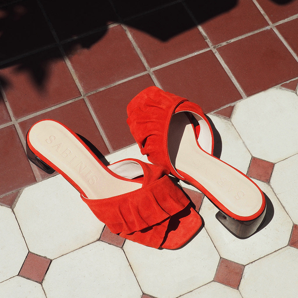 Par de sandalias Calm Red de ante rojo en escena lifestyle sobre suelo de baldosas, iluminación natural de Sabinis.